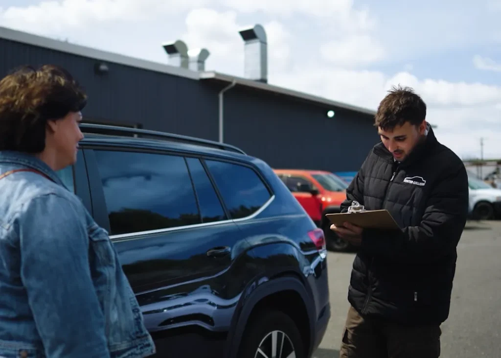 Person discussing with clipboard by car.